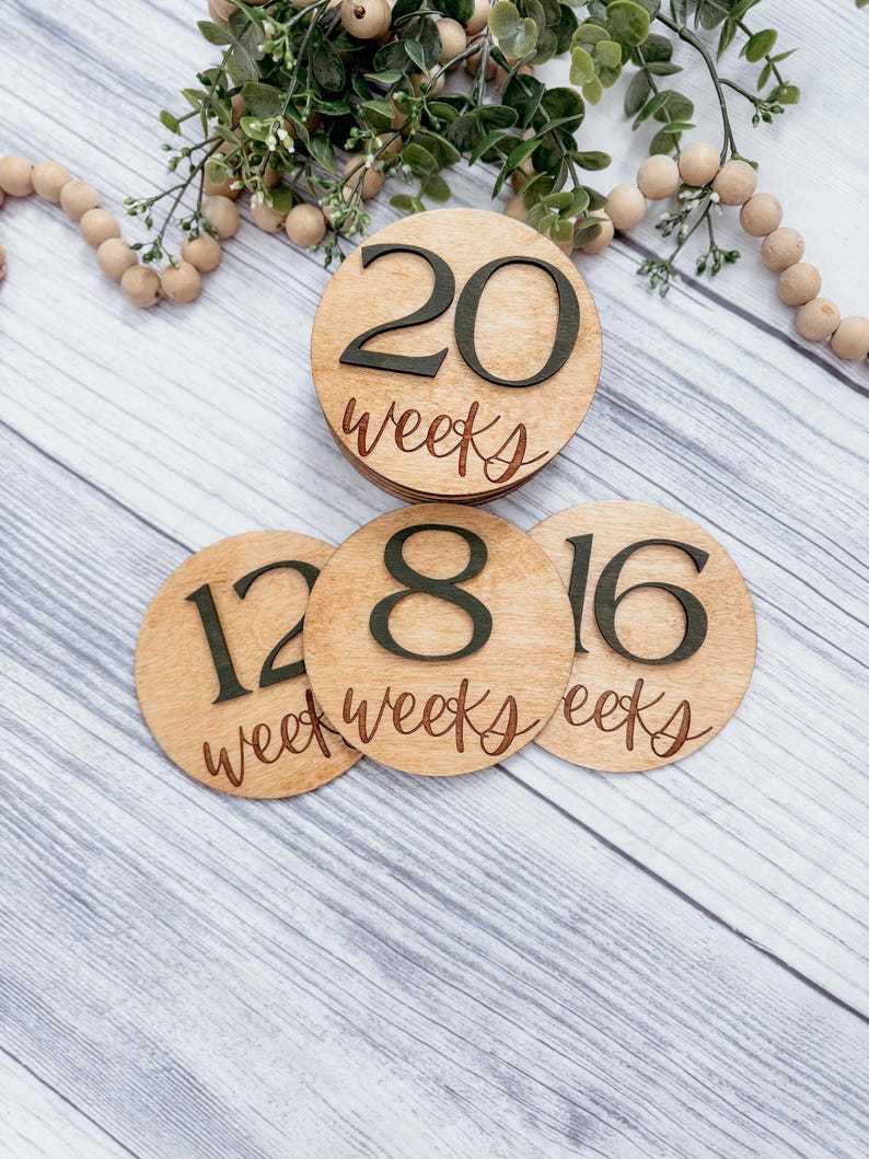 May include: Three wooden circles with numbers and the word "weeks" written on them. The numbers are 12, 18, and 20. The circles are stacked on top of each other.