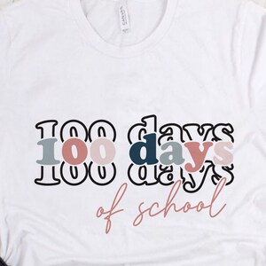 Puede incluir: Camiseta blanca con el texto "100 días de escuela" en letras negras delineadas con relleno rosa, azul y gris. El texto está en un estilo superpuesto y apilado.