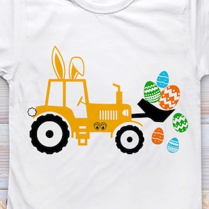Könnte beinhalten: Weißes T-Shirt mit einem gelben Traktor-Design, komplett mit Hasenohren und einem Eimer voller Ostereier. Der Traktor hat schwarze Räder und Ostermotive. Das Shirt hat den Text "BLUE OCEAN SVG PNG DXF JPG EPS".