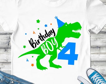 May include: A white t-shirt with a green dinosaur wearing a blue party hat. The dinosaur is holding a blue number 4. The text "Birthday Boy" is written in black above the dinosaur. There are small stars and squares in orange, blue, and green scattered around the dinosaur.