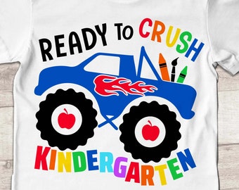 Puede incluir: Un camión monstruo azul con llamas y una manzana roja en cada neumático. El camión lleva útiles de arte, incluyendo crayones, pinceles y un lápiz. El texto "READY TO CRUSH KINDERGARTEN" está escrito en colores arcoíris alrededor del camión.