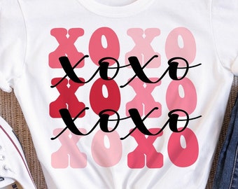 May include: White t-shirt featuring a graphic design of the word "XOXO" repeated four times in a gradient of pink and red colours.