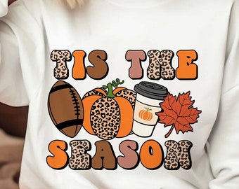 May include: White sweatshirt with the text "Tis the Season" in orange, brown, and pink letters with a leopard print design. The text is surrounded by a football, a pumpkin, a coffee cup, and a fall leaf.