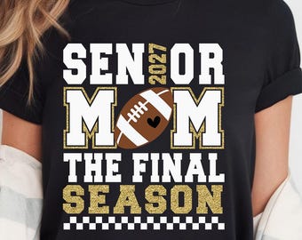May include: A black t-shirt featuring a graphic design with the text SENIOR 2027 MOM THE FINAL SEASON. The design includes a brown football with a small black heart, white lettering with gold glitter outlines, and a black and white checkered border.