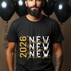 Peut inclure: T-shirt noir avec l'inscription "2026 New Year New Grace New Praise" en or et blanc. Le t-shirt est de style col rond et est port&eacute; par une personne. Des ballons noirs sont en arri&egrave;re-plan.