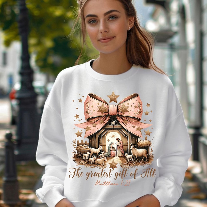 May include: White sweatshirt with a pink bow and a nativity scene with the text "The greatest gift of all Matthew 1:21".