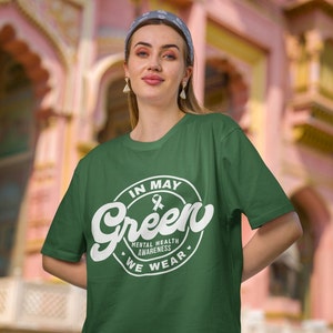 May include: Green t-shirt with a white circle graphic that says "In May We Wear Green" with a white ribbon inside the circle. The graphic also includes the words "Mental Health Awareness".