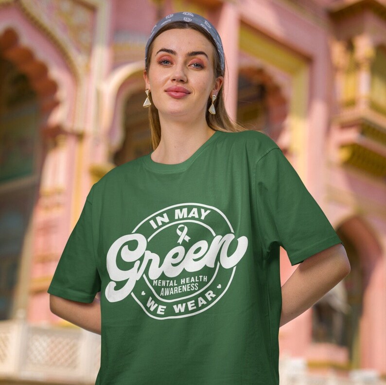 May include: Green t-shirt with a white circle graphic that says "In May We Wear Green" with a white ribbon inside the circle. The graphic also includes the words "Mental Health Awareness".