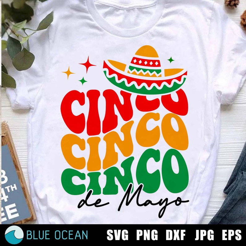 May include: A white t-shirt featuring a red, yellow and green graphic that reads "Cinco Cinco Cinco de Mayo" with a sombrero on top.
