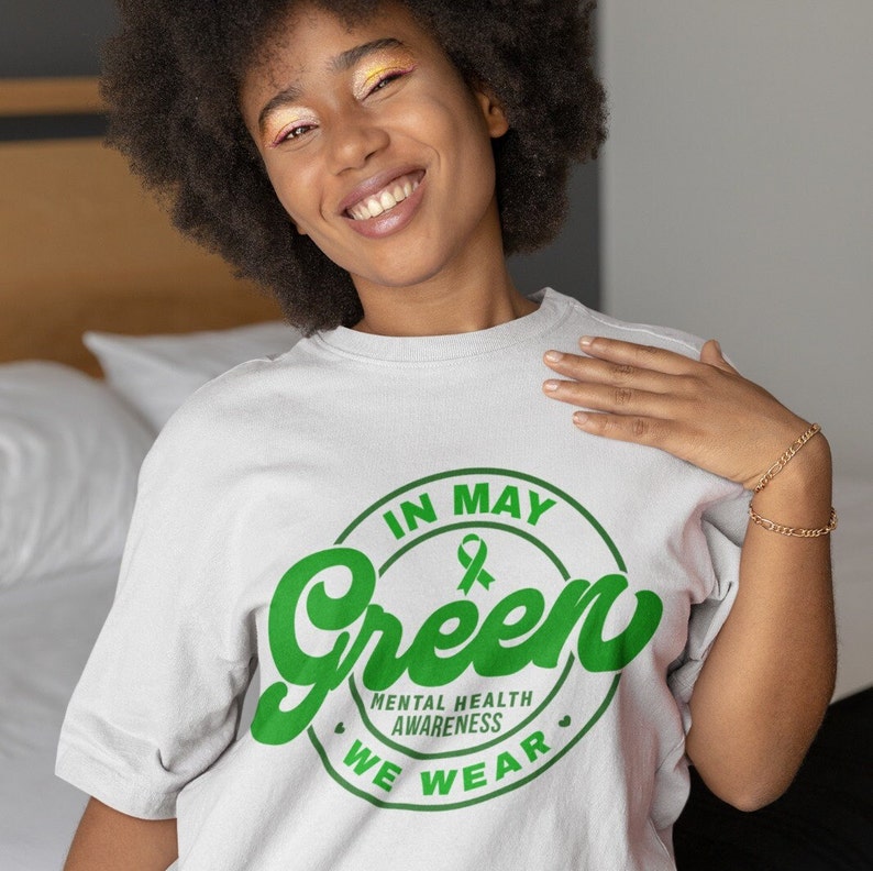 May include: A white t-shirt with a green circle graphic that says "In May We Wear Green" with a green ribbon inside the circle. The text "Mental Health Awareness" is written below the circle.