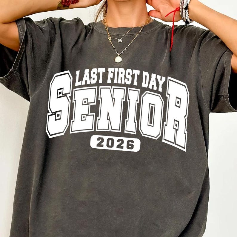 May include: Dark grey t-shirt featuring the text "LAST FIRST DAY SENIOR 2026" in white, block lettering. The shirt has a vintage appearance. A casual, comfortable top for the graduating class of 2026.