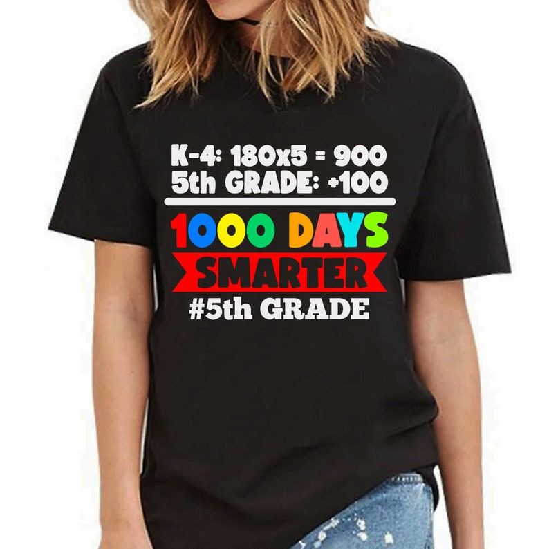 K&ouml;nnte beinhalten: Schwarzes T-Shirt mit dem Text "K-4: 180x5 = 900 5th GRADE: +100 1000 DAYS SMARTER #5th GRADE" in Wei&szlig;, Rot, Blau, Gelb und Gr&uuml;n. Das Shirt hat einen Rundhalsausschnitt und kurze &Auml;rmel.