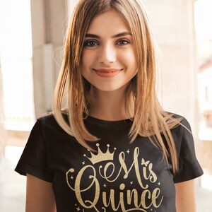 May include: A black t-shirt with a gold glitter design that says "#esMiQuince" with a crown above the text.