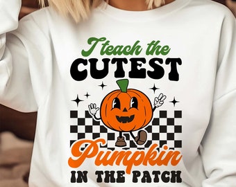 May include: White sweatshirt with a green and black graphic that says "I teach the cutest pumpkin in the patch". The graphic features a cartoon pumpkin with a smiling face and arms and legs.