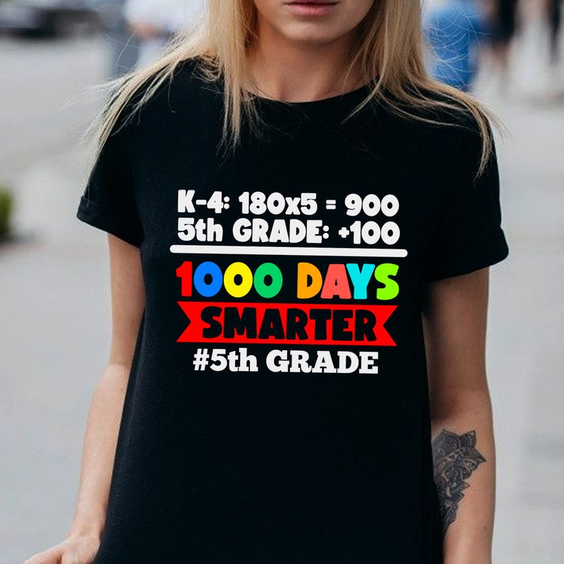 K&ouml;nnte beinhalten: Schwarzes T-Shirt mit dem Text "K-4: 180x5 = 900, 5th GRADE: +100, 1000 DAYS SMARTER, #5th GRADE" in Wei&szlig;, Rot, Blau und Gr&uuml;n. Das T-Shirt hat einen Rundhalsausschnitt.