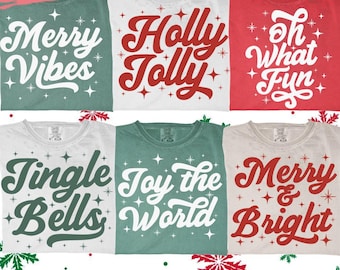 Könnte beinhalten: Sechs Weihnachtsshirts in verschiedenen Farben. Jedes Shirt zeigt einen anderen festlichen Satz in einer kräftigen Schriftart, wie "Merry Vibes" und "Holly Jolly". Die Shirts sind mit Sternen und Schneeflocken verziert.