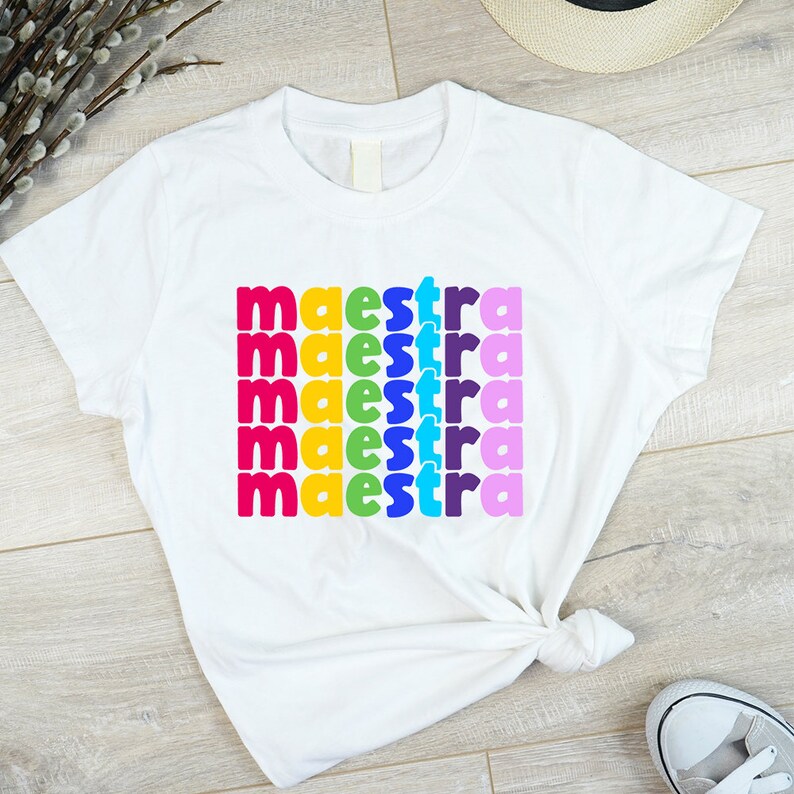 May include: White t-shirt with the word "maestra" repeated five times in rainbow colours.