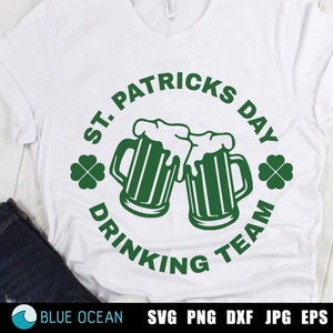 Może przedstawiać: Biała koszulka z zielonym kołem. Koło zawiera napis "St. Patricks Day Drinking Team" i dwa zielone kufle piwa, które się zderzają. Po obu stronach koła znajdują się zielone koniczyny.