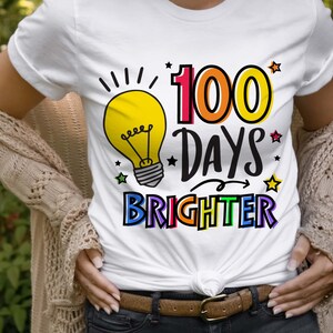 Peut inclure: T-shirt blanc avec un graphique d'ampoule et le texte "100 jours plus lumineux" en couleurs arc-en-ciel.