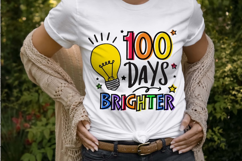 Peut inclure: T-shirt blanc avec un graphique d'ampoule et le texte "100 jours plus lumineux" en couleurs arc-en-ciel.