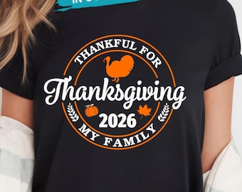 May include: A black t-shirt featuring a circular orange graphic with a turkey, a pumpkin, and a maple leaf. The text reads Thankful for Thanksgiving 2026 My Family. The design includes wheat stalks and is centered on the chest of the garment.