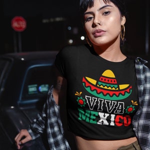 May include: A black crop top with a graphic of a sombrero and the text "Viva Mexico" in green, red, and white. The shirt is being worn by a person with a nose ring and earrings.