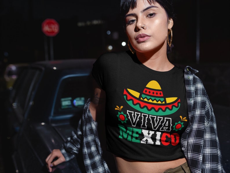May include: A black crop top with a graphic of a sombrero and the text "Viva Mexico" in green, red, and white. The shirt is being worn by a person with a nose ring and earrings.