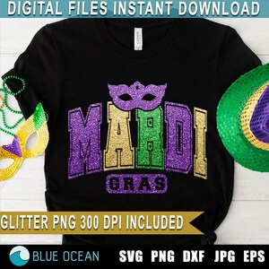May include: A black t-shirt with a purple, green, and gold glitter design that says "Mardi Gras" with a purple glitter mask above the text. The design is on a black t-shirt.