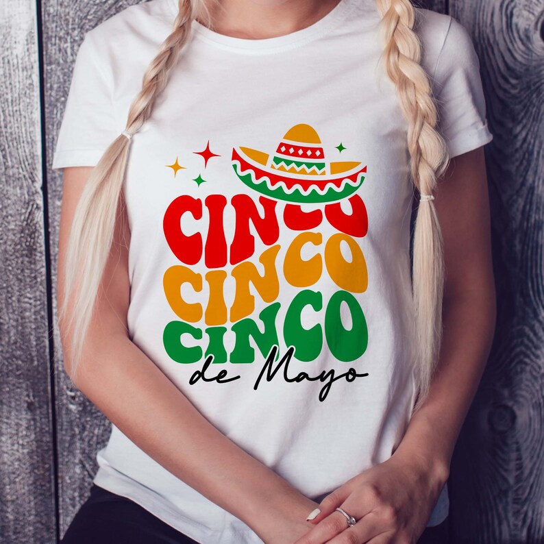 May include: White t-shirt featuring a colourful graphic design that reads "Cinco Cinco Cinco de Mayo" with a sombrero on top.