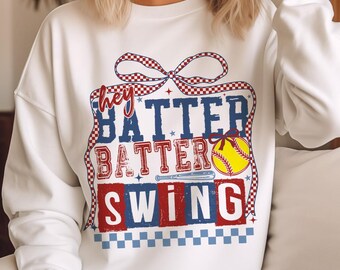 Może przedstawiać: Biała bluza z czerwono-biało-niebieskim nadrukiem graficznym z napisem "Hey Batter Batter Swing" oraz grafiką przedstawiającą piłkę baseballową i kij.