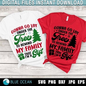 May include: Two Christmas-themed t-shirt designs. The white t-shirt has green text that reads "Gonna go lay under the tree to remind my family that I'm a gift". The red t-shirt has black text that reads "Gonna go lay under the tree to remind my family that I'm a gift".