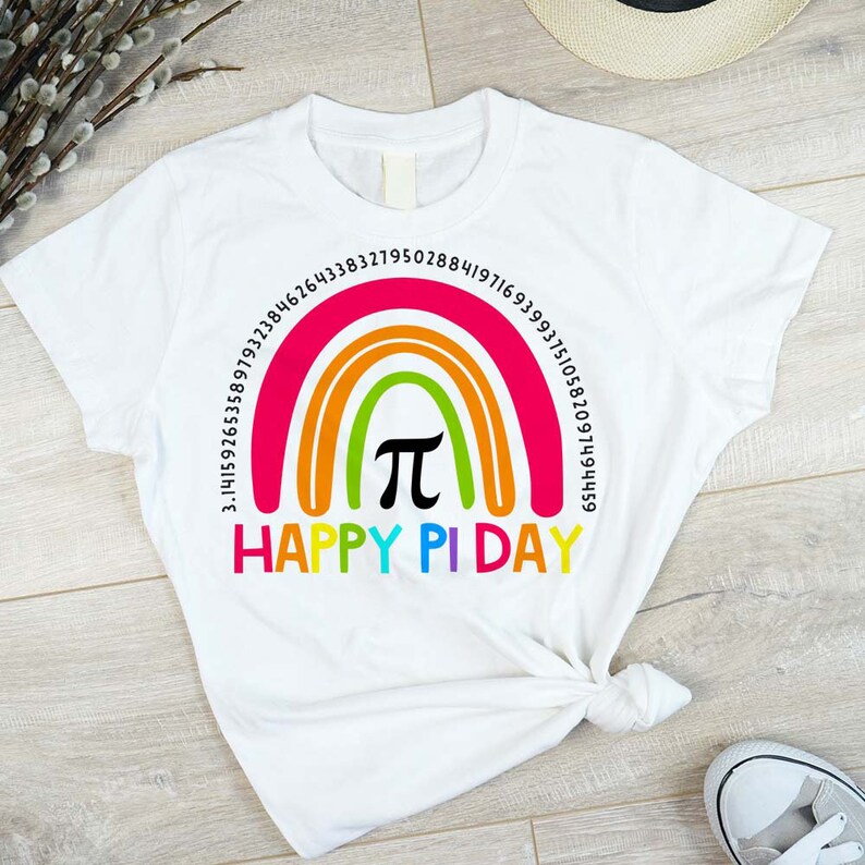 May include: White t-shirt with a rainbow design and the pi symbol in the centre. The words "HAPPY PI DAY" are printed below the rainbow. Numbers representing pi's value are arched above the rainbow. A fun, colourful design.