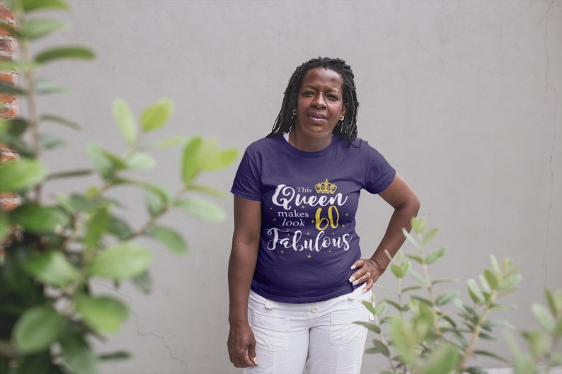 Op de afbeelding: Een vrouw draagt een paars T-shirt met de tekst "This Queen makes 60 look Fabulous" in gouden letters en een gouden kroonafbeelding.