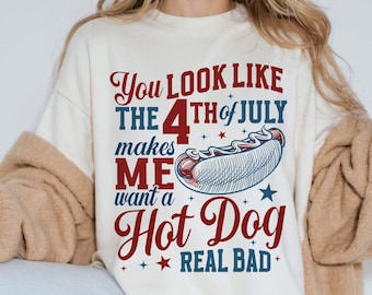 May include: A white t-shirt with a red, white, and blue graphic design that says "You look like the 4th of July makes me want a Hot Dog real bad".