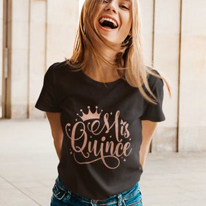 May include: A black t-shirt with a rose gold crown and the text "Es Mi Quince" in a cursive font.