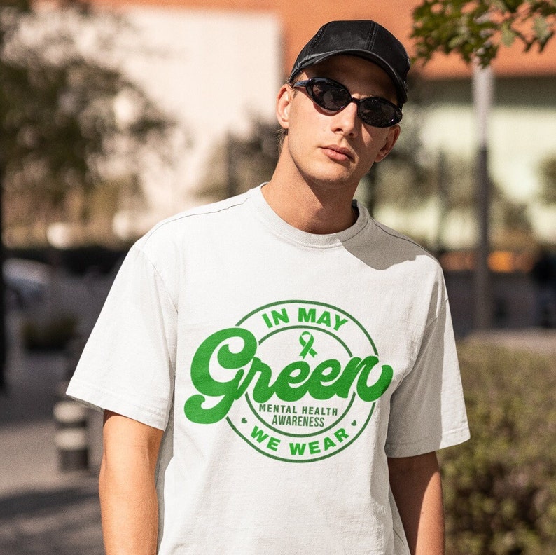 May include: White t-shirt with a green circle graphic that says "In May We Wear Green" and has a green ribbon inside the circle. The text "Mental Health Awareness" is written below the circle.