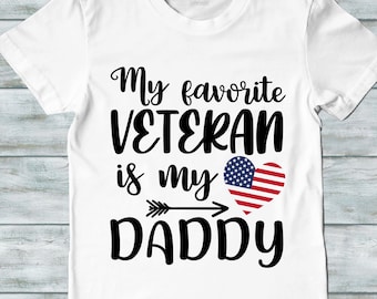 May include: White t-shirt with black text that reads "My favorite VETERAN is my DADDY" with an arrow pointing to a red heart with an American flag design.