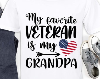 May include: A white t-shirt with black text that reads "My favorite VETERAN is my GRANDPA" with an arrow pointing to a red, white, and blue heart with an American flag design.