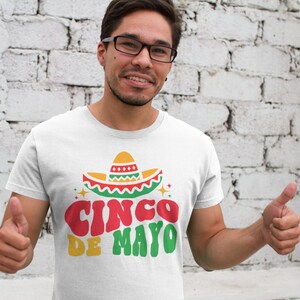 May include: White t-shirt with a green, red, and yellow sombrero graphic and the text "Cinco de Mayo" in a retro font.