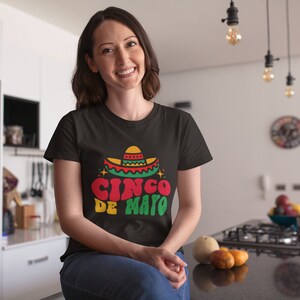 May include: A woman wearing a black t-shirt with a colorful graphic of a sombrero and the text "Cinco de Mayo".