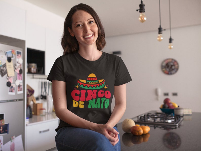 May include: A woman wearing a black t-shirt with a colorful graphic of a sombrero and the text "Cinco de Mayo".