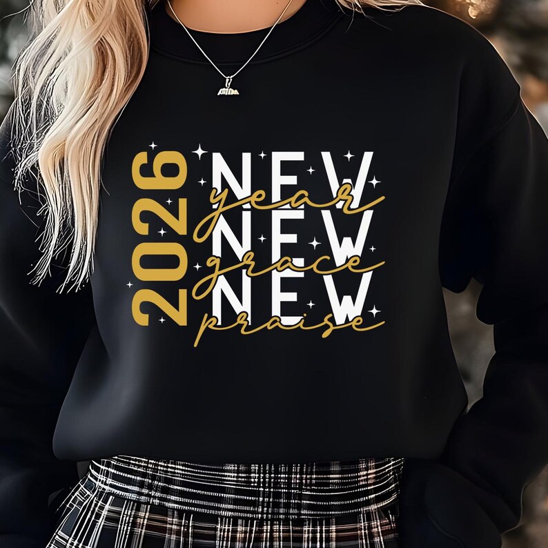 Peut inclure: Sweat-shirt noir avec l'inscription "2026 New Year New Grace New Praise" en or et blanc. Le motif comprend des &eacute;toiles et une police script. V&ecirc;tement de style d&eacute;contract&eacute;.