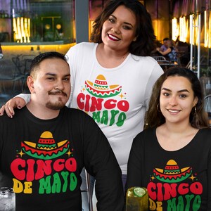May include: Three people wearing black and white shirts with a Cinco de Mayo design. The shirts feature a sombrero with red, yellow, and green colors and the text "Cinco de Mayo".