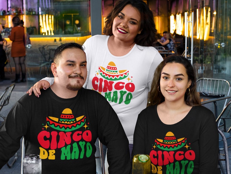May include: Three people wearing black and white shirts with a Cinco de Mayo design. The shirts feature a sombrero with red, yellow, and green colors and the text "Cinco de Mayo".