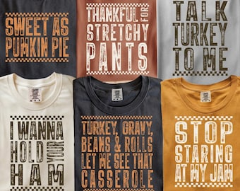 May include: A collection of six crew neck t-shirts in various colors, each featuring a unique graphic design with text and a checkered border. The shirts display phrases including Sweet as Pumpkin Pie, Thankful for Stretchy Pants, Talk Turkey to Me, I Wanna Hold Your Ham, Turkey, Gravy, Beans & Rolls Let Me See That Casserole, and Stop Staring at My Jam.