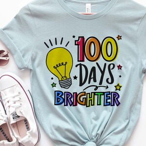 Peut inclure: Un t-shirt bleu clair avec un graphique d'ampoule color&eacute; et le texte "100 jours plus lumineux".