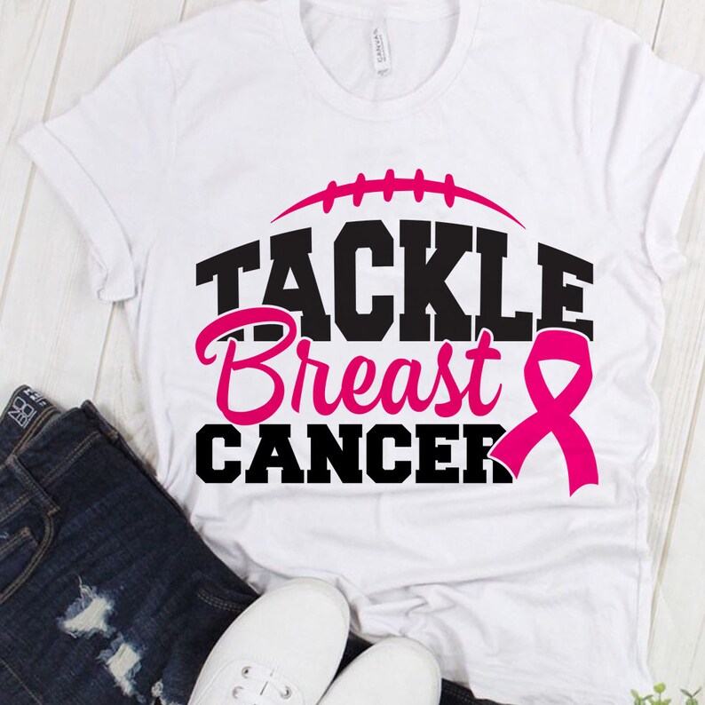 Peut inclure: T-shirt blanc avec un texte noir qui dit "Tackle Breast Cancer" et un ruban rose. Un graphique de football est au-dessus du texte.