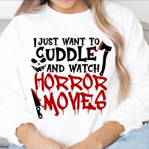 May include: White sweatshirt with a black and red graphic print that says "I just want to cuddle and watch horror movies". The graphic includes a cartoon axe, a knife, and a scary face.