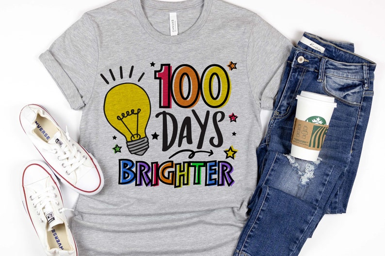 Peut inclure: Un t-shirt gris avec un graphique d'ampoule et le texte "100 Days Brighter" en couleurs arc-en-ciel. Le texte est soulign&eacute; en noir.