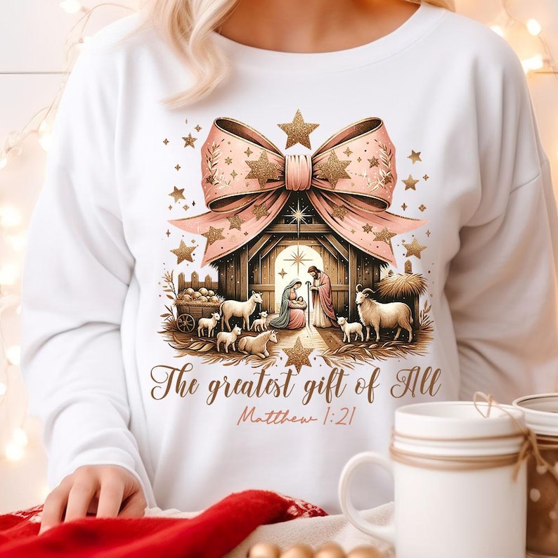 May include: White sweatshirt with a pink and gold bow and a nativity scene with the text "The greatest gift of all Matthew 1:21".